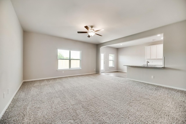 unfurnished living room with baseboards, a ceiling fan, and light carpet