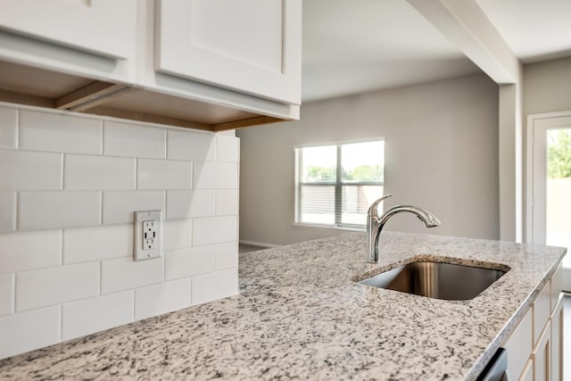 kitchen with light stone counters, a sink, white cabinets, and a wealth of natural light