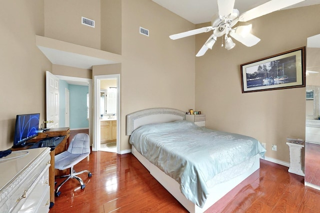bedroom featuring wood finished floors, a towering ceiling, baseboards, a desk, and connected bathroom