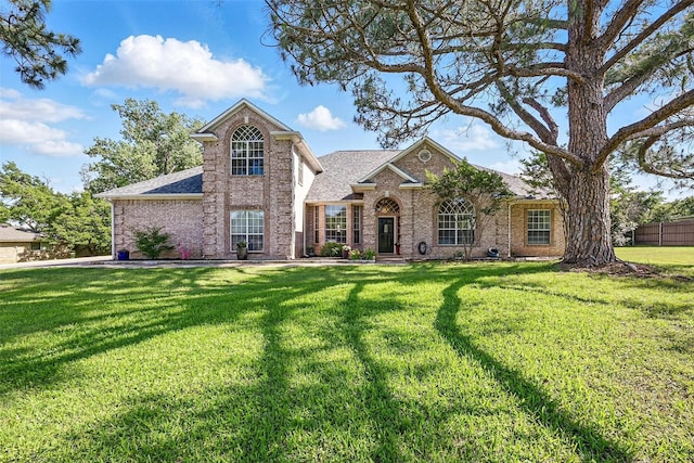 traditional home with brick siding, a front yard, and a shingled roof