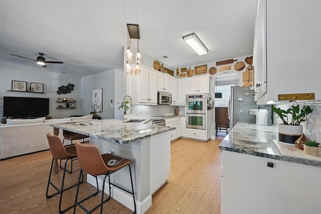 kitchen featuring stainless steel appliances, a peninsula, a sink, a breakfast bar, and stone counters