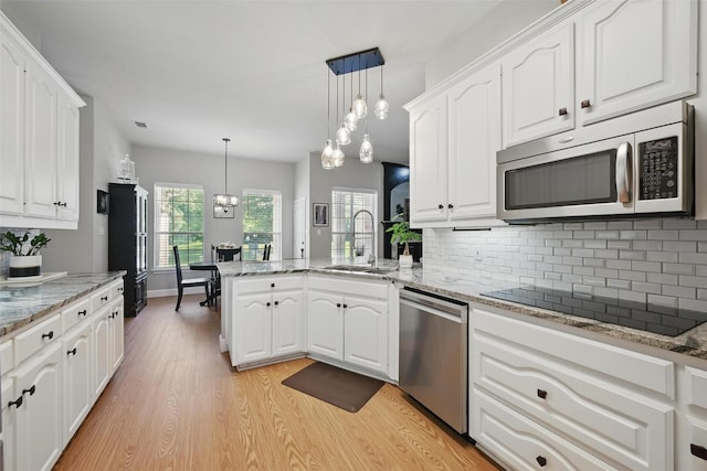 kitchen featuring stainless steel appliances, a sink, a peninsula, light wood-type flooring, and white cabinetry