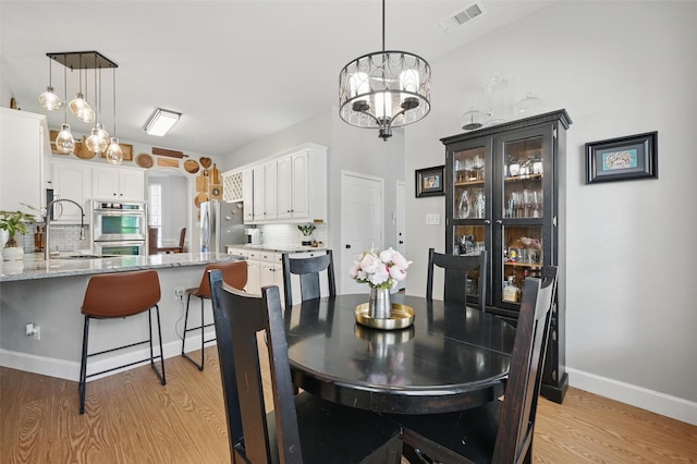 dining area with light wood-type flooring, a chandelier, and baseboards