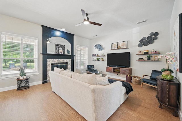 living room featuring a ceiling fan, a glass covered fireplace, light wood-style flooring, and baseboards