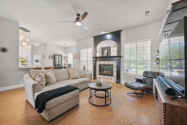living area with a ceiling fan, wood finished floors, baseboards, a fireplace, and a chandelier