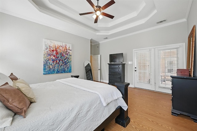 bedroom featuring a tray ceiling, access to outside, light wood-type flooring, crown molding, and a ceiling fan