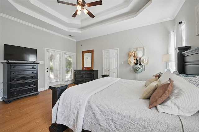 bedroom with a raised ceiling, wood finished floors, access to exterior, crown molding, and ceiling fan