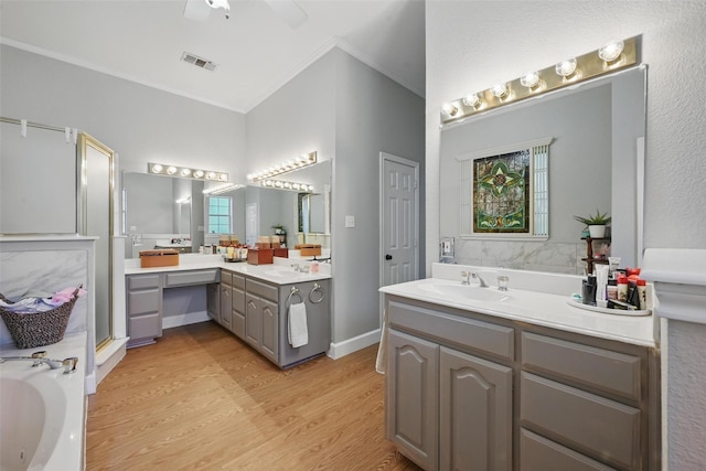 bathroom with ornamental molding, two vanities, wood finished floors, a bath, and ceiling fan