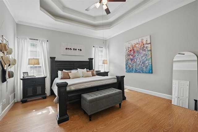 bedroom featuring arched walkways, light wood-style flooring, a raised ceiling, ornamental molding, and ceiling fan