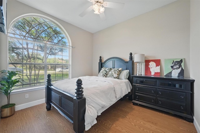 bedroom with multiple windows, baseboards, vaulted ceiling, wood finished floors, and ceiling fan