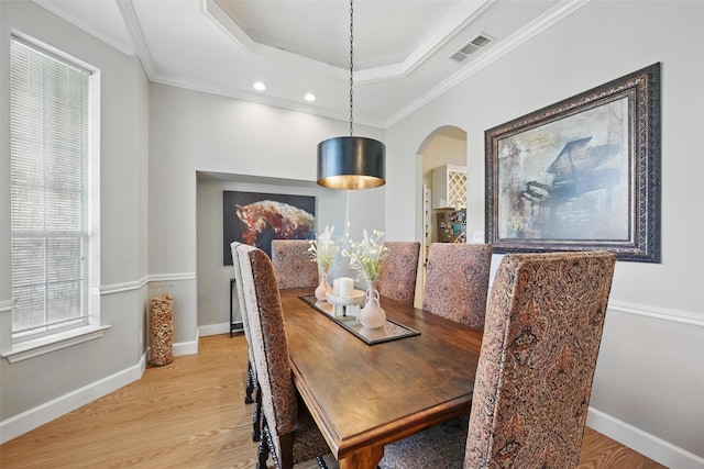 dining area featuring arched walkways, light wood-style flooring, a tray ceiling, ornamental molding, and baseboards
