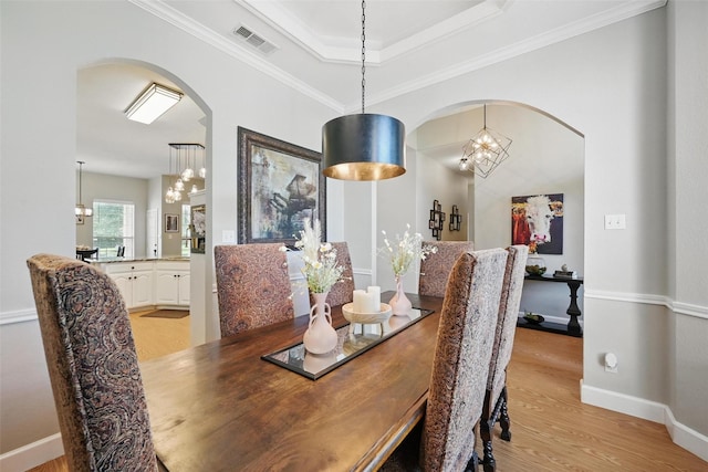 dining area with a chandelier, light wood finished floors, arched walkways, and crown molding