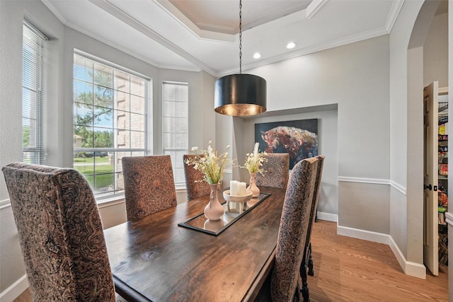 dining room featuring wood finished floors, arched walkways, a tray ceiling, baseboards, and crown molding