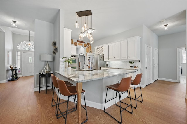 kitchen featuring stainless steel fridge, a peninsula, a kitchen bar, white cabinets, and healthy amount of natural light