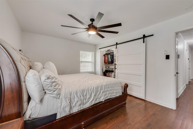 bedroom with a ceiling fan, dark wood finished floors, a barn door, baseboards, and a closet