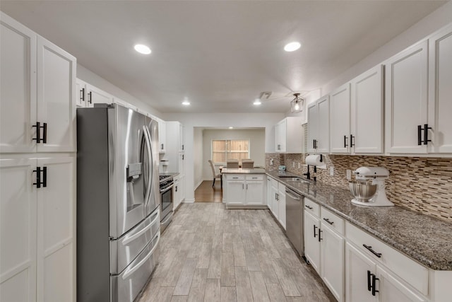 kitchen with appliances with stainless steel finishes, tasteful backsplash, white cabinets, a peninsula, and light wood-style floors