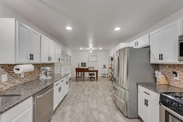kitchen with decorative backsplash, appliances with stainless steel finishes, light wood-style floors, dark stone counters, and white cabinetry