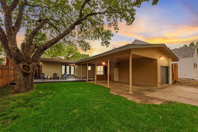 back of property at dusk with ceiling fan, french doors, a lawn, fence, and concrete driveway