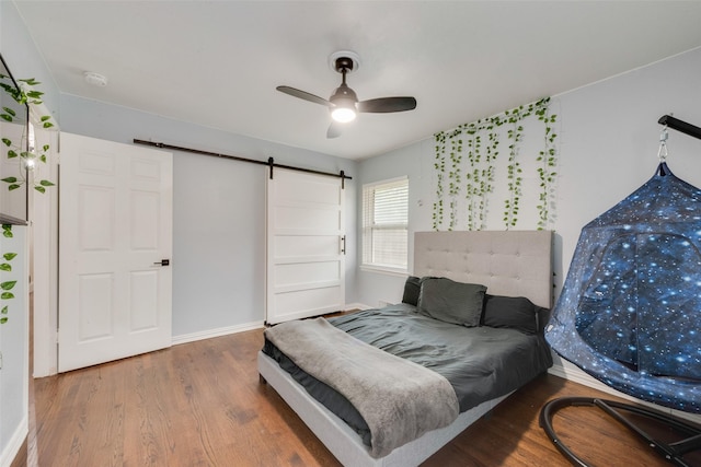 bedroom with baseboards, ceiling fan, a barn door, and wood finished floors
