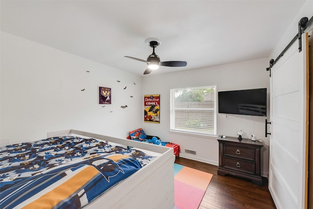bedroom featuring visible vents, wood finished floors, baseboards, a barn door, and a ceiling fan