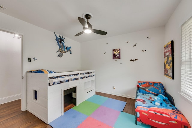 bedroom featuring baseboards, a ceiling fan, wood finished floors, and multiple windows