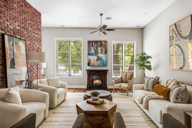 living room featuring ceiling fan, visible vents, a warm lit fireplace, light wood-style floors, and a wealth of natural light