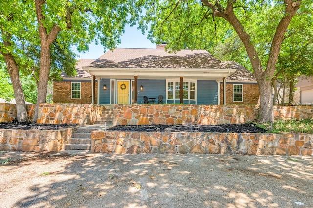 view of front of house with covered porch, brick siding, a shingled roof, and a chimney