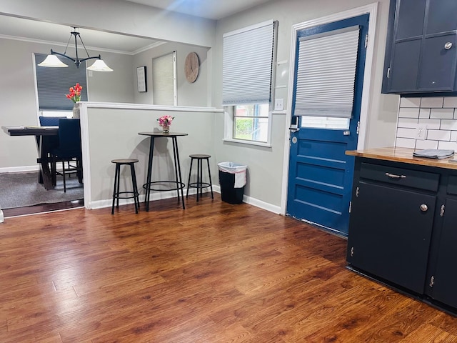 kitchen with dark wood finished floors, decorative light fixtures, baseboards, tasteful backsplash, and ornamental molding