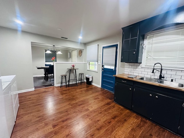 kitchen with a sink, washing machine and clothes dryer, dark cabinetry, decorative backsplash, and dark wood finished floors