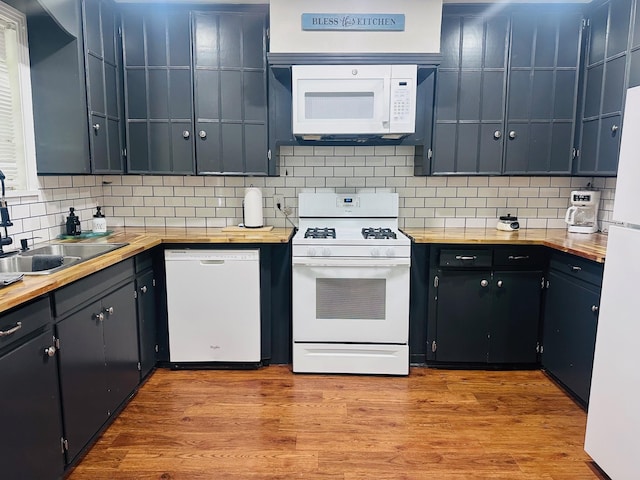 kitchen with white appliances, backsplash, a sink, and wood finished floors