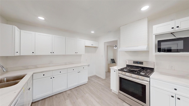 kitchen with gas stove, a sink, white cabinets, light wood-style floors, and under cabinet range hood