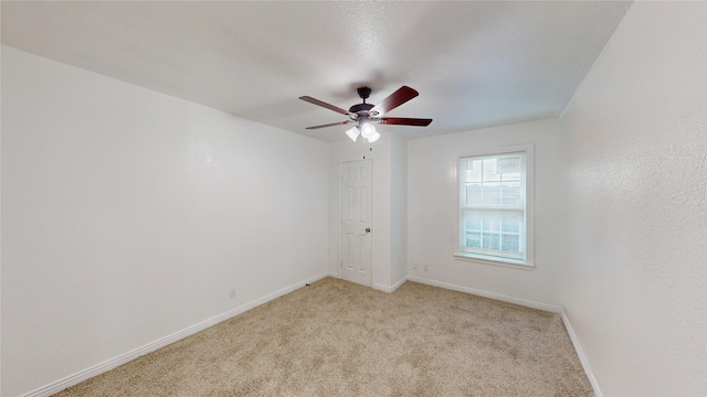 empty room with baseboards, a ceiling fan, and light carpet