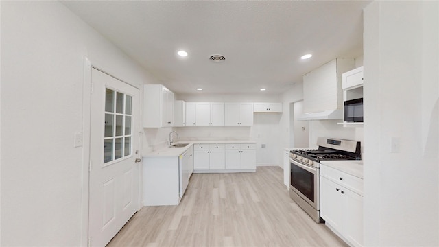 kitchen featuring stainless steel gas stove, a sink, light countertops, light wood-style floors, and white cabinetry