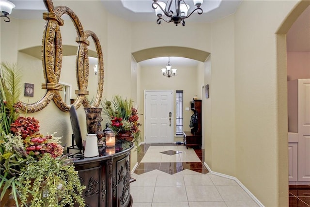 tiled foyer featuring an inviting chandelier, arched walkways, baseboards, and a high ceiling