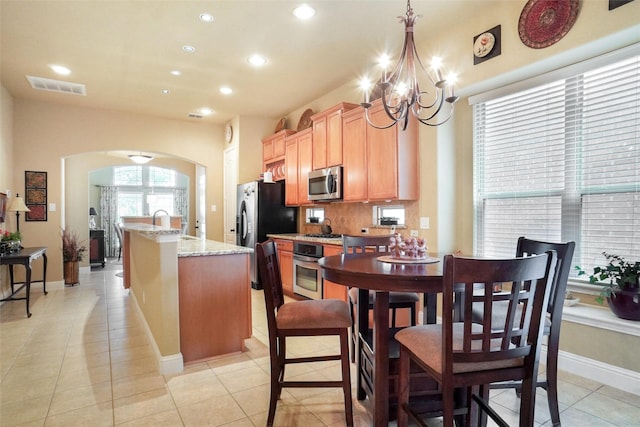 kitchen with appliances with stainless steel finishes, arched walkways, a chandelier, recessed lighting, and an island with sink