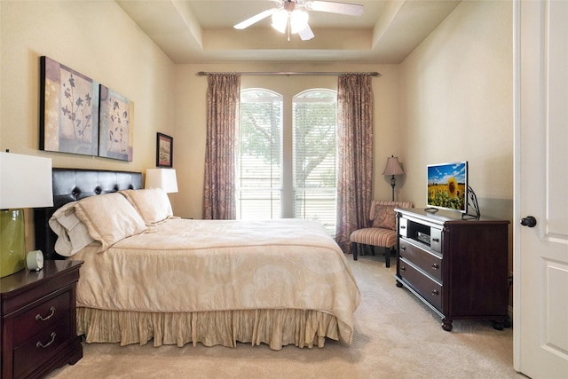bedroom with light carpet, a tray ceiling, and ceiling fan
