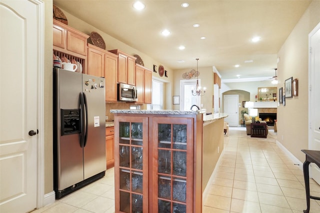 kitchen with appliances with stainless steel finishes, light tile patterned floors, a warm lit fireplace, recessed lighting, and a chandelier