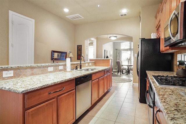 kitchen featuring stainless steel appliances, a sink, arched walkways, light stone countertops, and light tile patterned floors