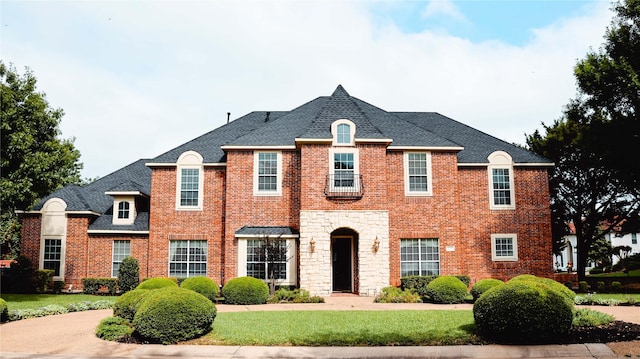 french country home with brick siding, a front lawn, stone siding, and roof with shingles