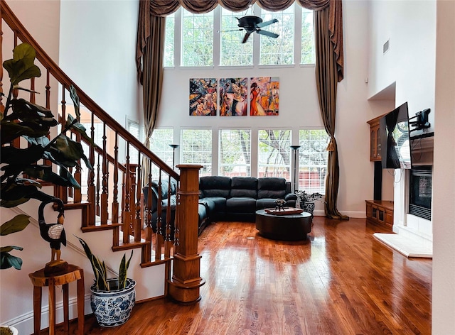 living area with a towering ceiling, wood finished floors, stairway, baseboard heating, and baseboards