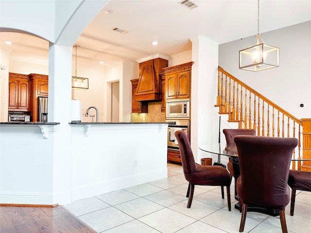 kitchen with stainless steel appliances, arched walkways, premium range hood, brown cabinets, and tasteful backsplash