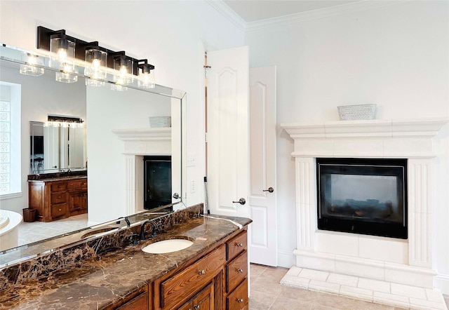 bathroom featuring a glass covered fireplace, crown molding, two vanities, and tile patterned floors
