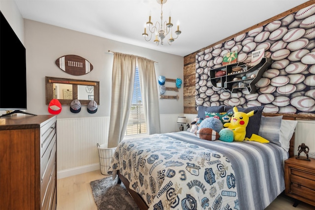 bedroom with a wainscoted wall, light wood-type flooring, and a chandelier