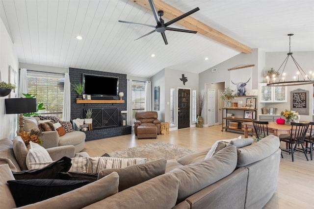 living area featuring a brick fireplace, beamed ceiling, ceiling fan with notable chandelier, recessed lighting, and light wood-style flooring
