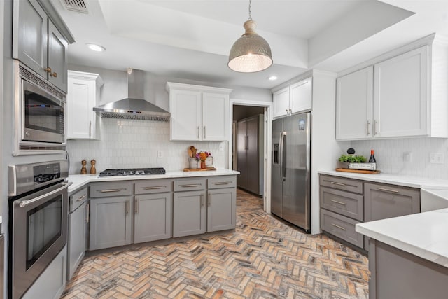 kitchen featuring light countertops, gray cabinets, wall chimney exhaust hood, stainless steel appliances, and backsplash
