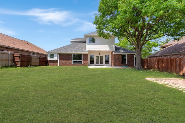 rear view of house featuring a shingled roof, brick siding, french doors, a fenced backyard, and a lawn