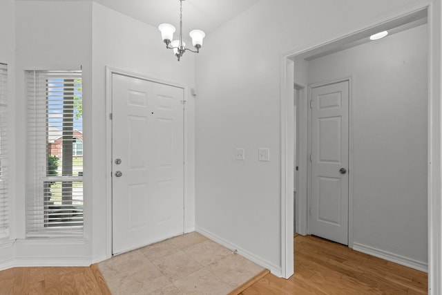 foyer featuring baseboards, light wood finished floors, and a chandelier