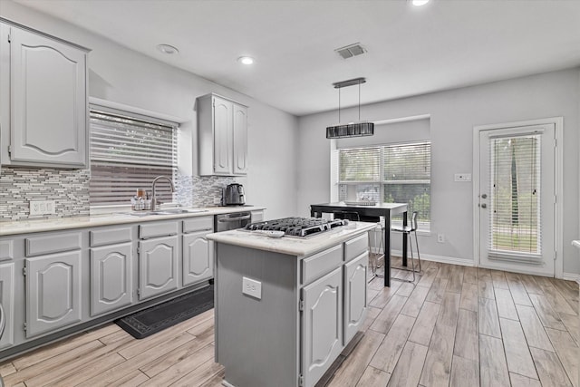 kitchen with decorative backsplash, a center island, a sink, light wood-style flooring, and appliances with stainless steel finishes