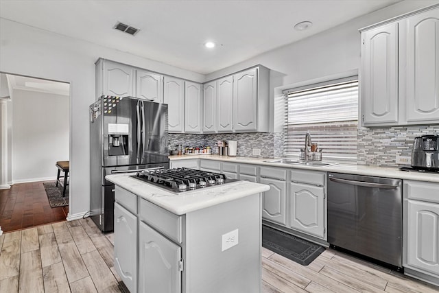 kitchen with a sink, stainless steel appliances, decorative backsplash, light wood-type flooring, and a kitchen island