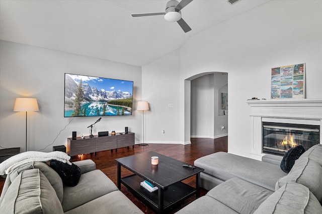 living area with arched walkways, a glass covered fireplace, a ceiling fan, wood finished floors, and lofted ceiling